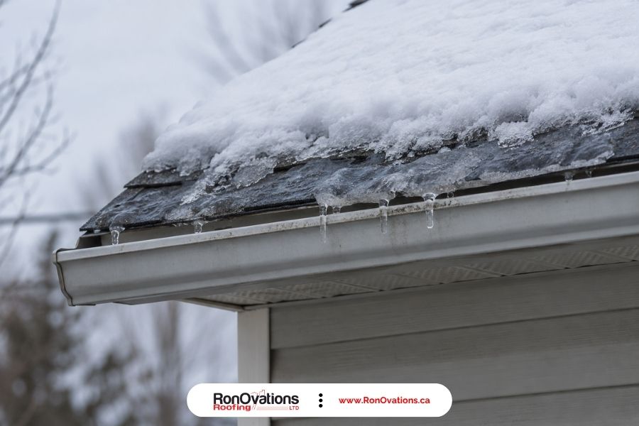 Snow at a residential roof edge with localized ice and short icicles near the gutter.